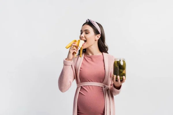 Joyful Pregnant Woman Eating Banana Holding Jar Canned Cucumbers Isolated — Stock Photo, Image