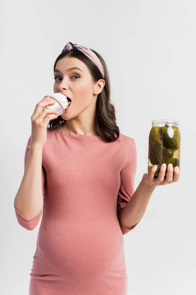 Young Pregnant Woman Eating Cupcake Holding Jar Pickled Cucumbers Isolated — Stock Photo, Image