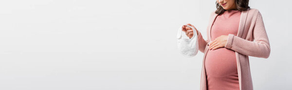 cropped view of pregnant woman holding small baby bib isolated on white, panoramic shot