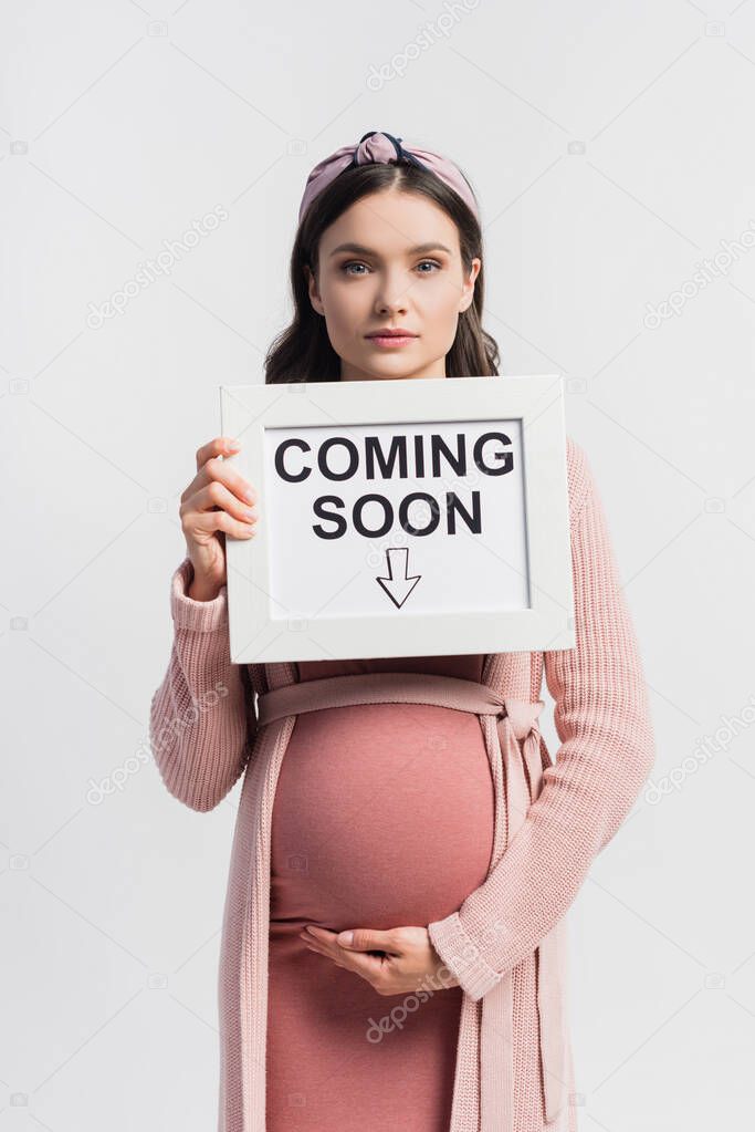 Pregnant woman holding board with coming soon lettering isolated on white