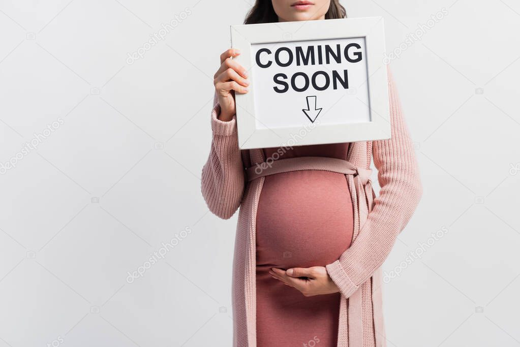 Cropped view of pregnant woman holding board with coming soon lettering isolated on white