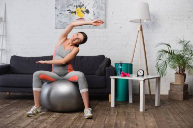 Spor kıyafetli neşeli hamile kadın oturma odasında spor paspasıyla egzersiz yapıyor. 