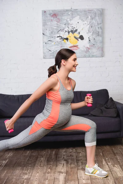 自宅でピンクのダンベルで運動する楽しい妊婦の姿を — ストック写真