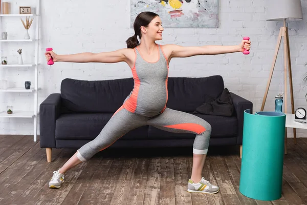 自宅でピンクのダンベルと運動しながら手を伸ばして立って楽しい妊娠中の女性 — ストック写真
