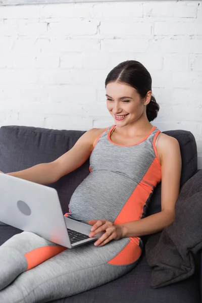 Fröhliche Sportliche Und Schwangere Frau Blickt Wohnzimmer Auf Laptop — Stockfoto