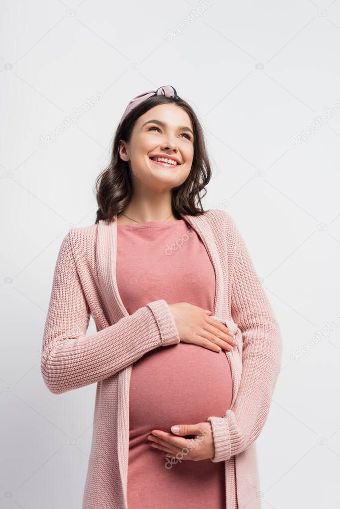 pregnant woman in cardigan and headband touching belly isolated on white