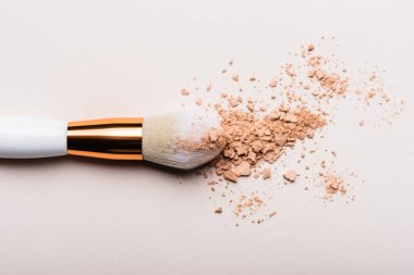 Bej arkaplanda yüz pudrası olan kozmetik fırçanın üst görünümü