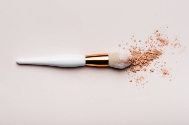 Bej arkaplanda yüz pudrası olan kozmetik fırçanın üst görünümü