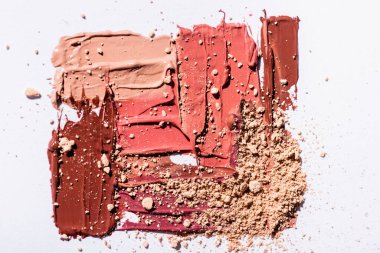 Beyaz arkaplanda pembe, bej ve kahverengi ruj fırça darbelerinin ve yüz pudrasının üst görünümü