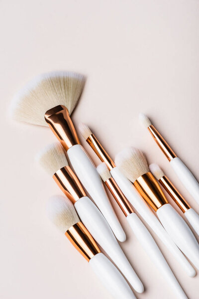 top view of white and golden cosmetic brushes set on beige background