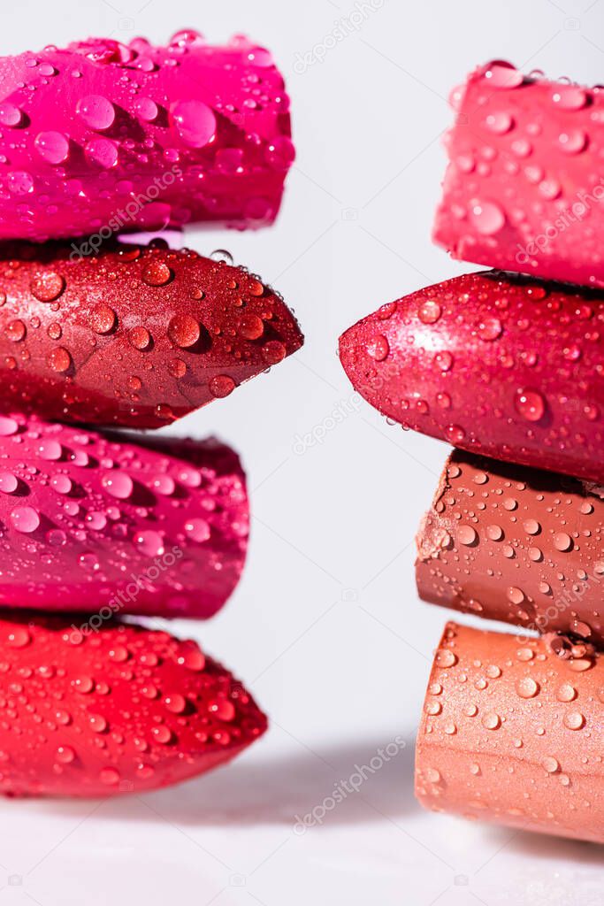 close up view of wet colorful lipsticks on white background