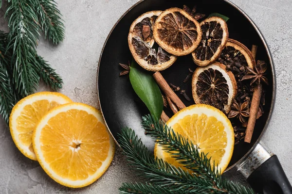 Top view of frying pan with spices, orange slices and pine branches