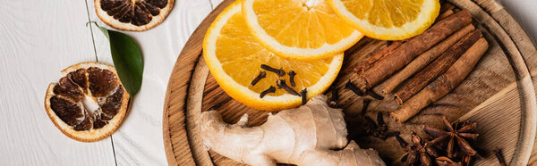 Panoramic shot of wooden plate with spices and fresh orange slices