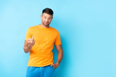 man in t-shirt standing with hand in pocket and showing middle finger on blue clipart