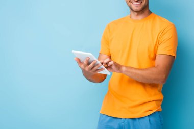 Mavi üzerine dijital tablet kullanan tişörtlü mutlu adamın kırpılmış görüntüsü