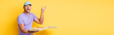 Mavi şapkalı bir adam elinde lezzetli pizzayla kutuda el kol hareketi yapıyor.