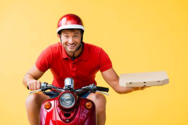 Kasklı neşeli teslimatçı kırmızı scooter sürüyor ve sarı üzerinde izole pizza kutusu tutuyor.