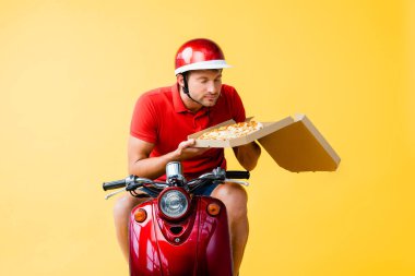 Kasklı teslimatçı kırmızı scooter sürüyor ve sarı kutudaki pizzanın kokusunu alıyor.