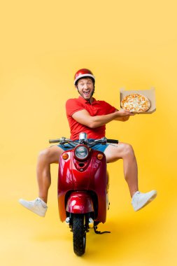 Kasklı heyecanlı teslimatçı scooter sürüyor ve sarı kutuda pizza tutuyor.