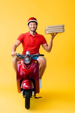 Kasklı mutlu teslimatçı scooter sürüyor ve sarı kutuda pizza kutuları tutuyor. 