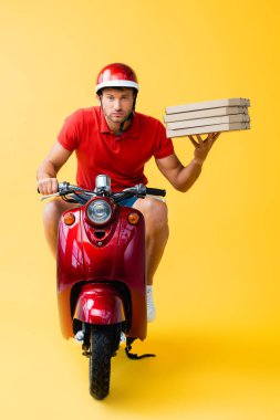 Kasklı teslimatçı scooter sürüyor ve sarı kutular üzerinde pizza kutuları tutuyor. 