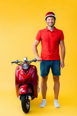 Kırmızı scooter 'ın yanında duran kasklı mutlu bir adam.