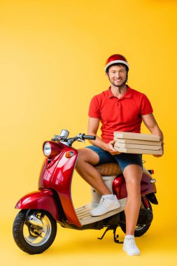 Kasklı mutlu teslimatçı elinde pizza kutusuyla motosikletin üzerinde otururken