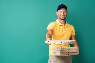 Sevinçli teslimatçı elini uzatmış, elinde pizza kutuları var.
