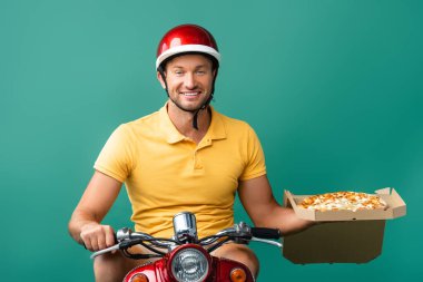 Kasklı gülümseyen teslimatçı scooter sürerken mavi kutuda lezzetli pizzalar tutuyor.