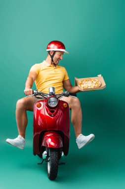 Kasklı, heyecanlı teslimatçı Scooter sürerken elinde lezzetli pizzalar, mavi kutuda.