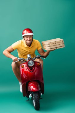 Kasklı teslimatçı, elinde pizza kutularıyla motosiklet sürerken dudak ısırıyor.