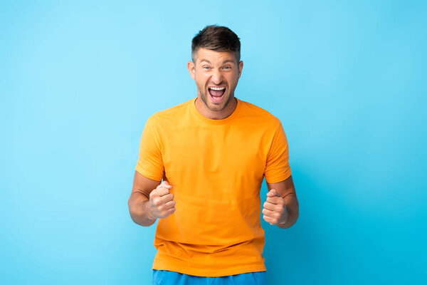 excited man with open mouth and clenched fists on blue
