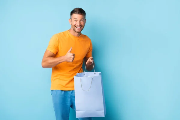 Glad Man Shirt Håller Shoppingväska Och Visar Tummen Upp Blå — Stockfoto