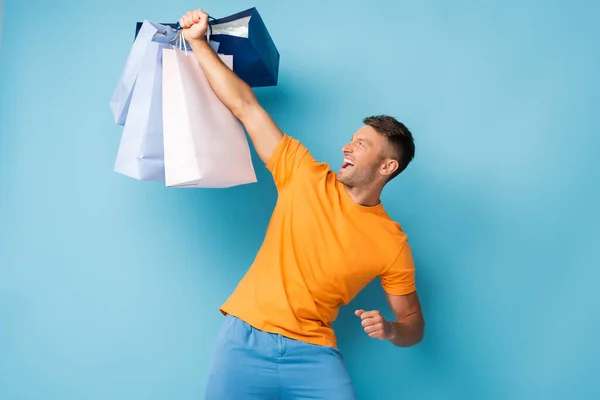 Excited Man Yellow Shirt Holding Shopping Bags Blue — Stock Photo, Image