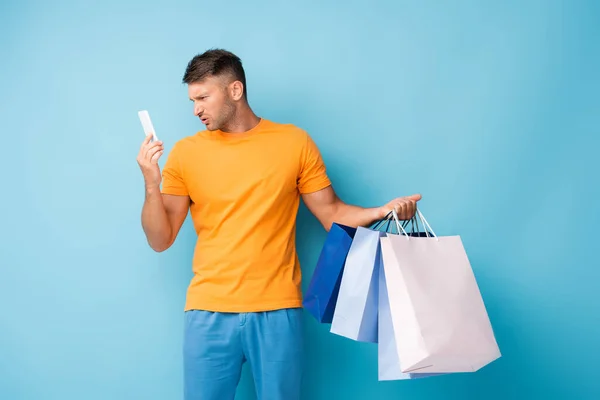 Šťastný Muž Drží Nákupní Tašky Při Pohledu Smartphone Modré — Stock fotografie