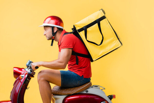 side view of delivery man with backpack riding red scooter on yellow