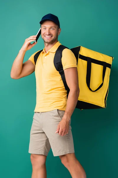 微笑的送货人背着黄色的背包 用蓝色的智能手机交谈 — 图库照片