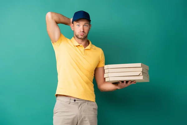 confused delivery man in cap holding pizza boxes on blue