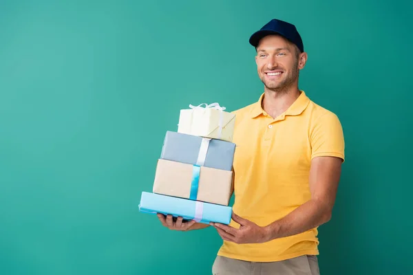 positive delivery man in cap holding wrapped presents on blue