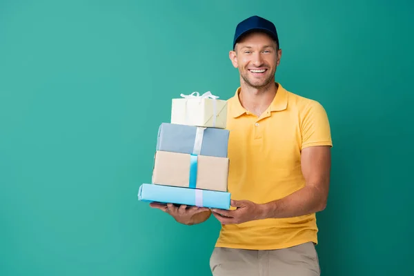smiling delivery man in cap holding wrapped presents on blue