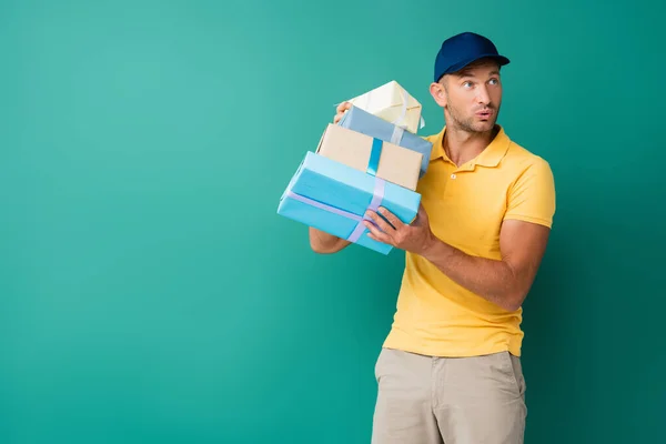 curious delivery man in cap holding wrapped presents on blue