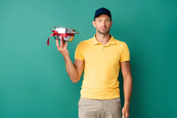 delivery man in cap holding saucepan with ribbon on blue