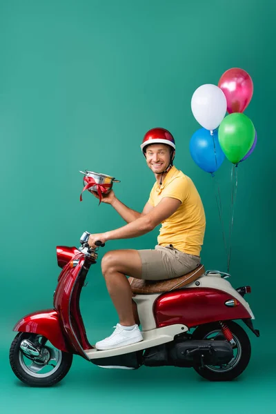 Szczęśliwy Dostawca Kasku Gospodarstwa Rondel Wstążką Podczas Jazdy Skuter Balonami — Zdjęcie stockowe