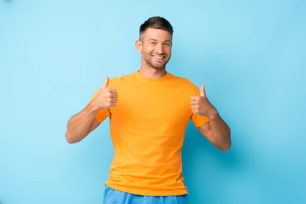 happy man in yellow t-shirt showing thumbs up on blue
