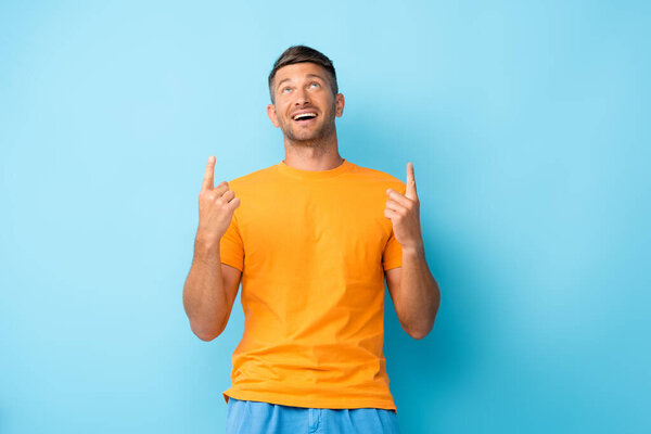 happy man in yellow t-shirt pointing with fingers and looking up on blue