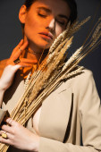 lighting on young woman in beige blazer holding barley spikelets on dark grey