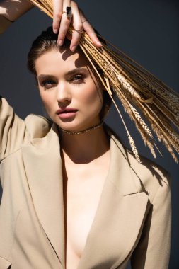 Spor ceketli kadın kameraya bakıyor ve koyu gri üzerinde buğday tutuyor.