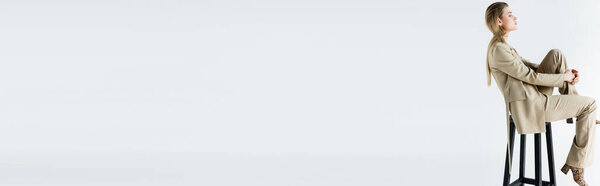 вид сбоку молодой модели в костюме, сидящей на табуретке на белом фоне, баннер