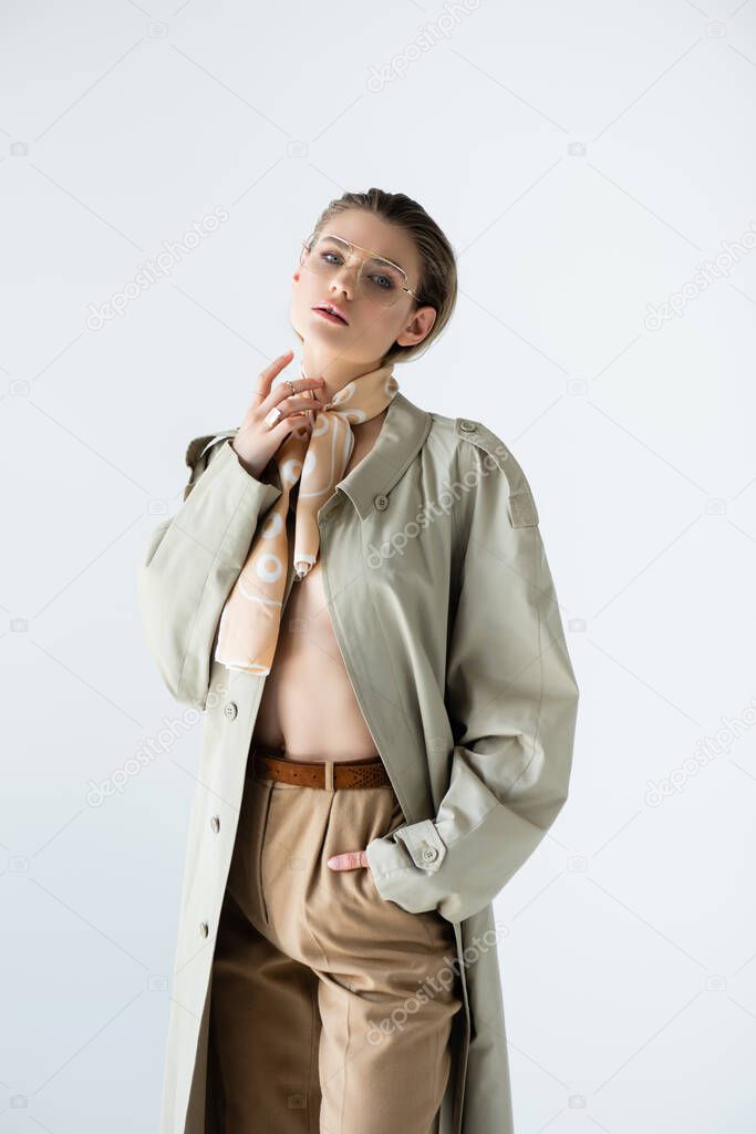 young model in glasses, trench coat and scarf posing isolated on white