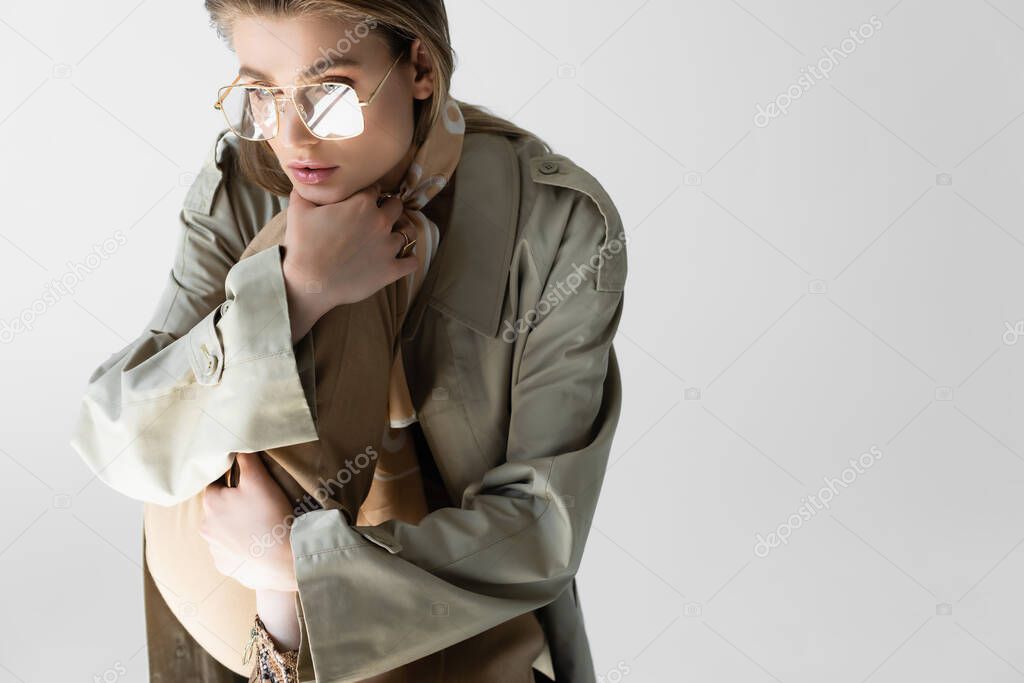 elegant young woman in trench coat, glasses and scarf posing isolated on white
